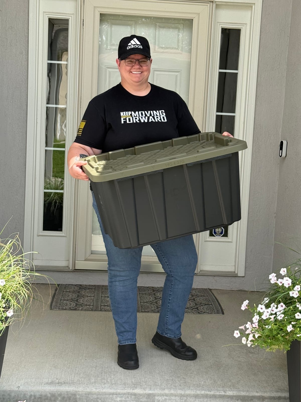Shelley from The Green Move KC on a front porch, holding one of our black totes with a green lid